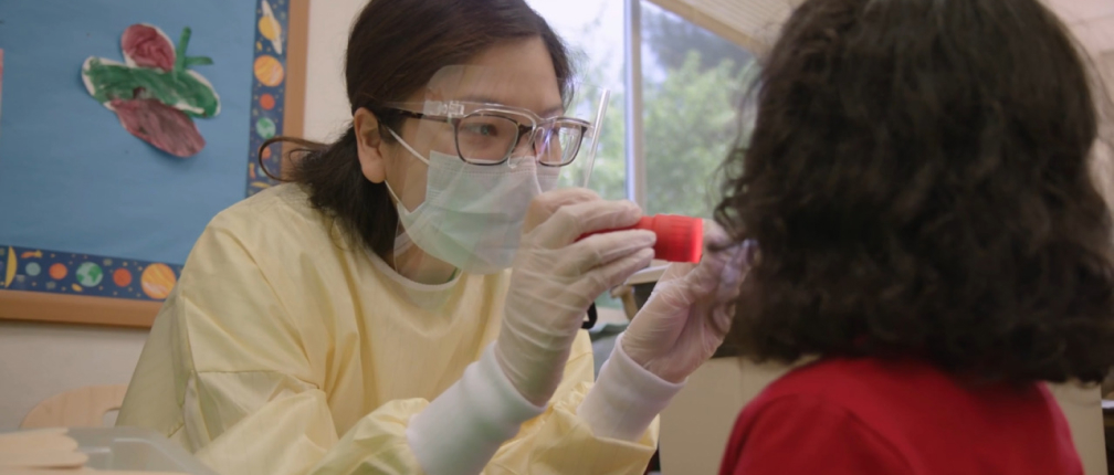 A woman in a lab coat gently inspects a child.