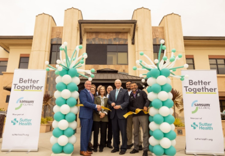 A diverse group of individuals posing in front of a building, holding colorful balloons.